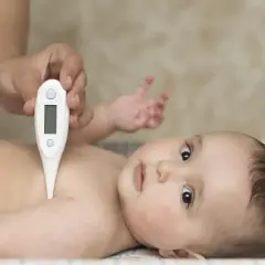Dziecko leży na plecach, a ręka rodzica mierzy mu temperaturę termometrem pod pachą. To jedno z miejsc, gdzie mierzyć temperaturę u malucha.