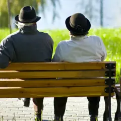 Dwie osoby w kapeluszach siedzą na ławce w parku, rozmawiając o najczęstszych chorobach w Polsce.