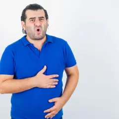 Mężczyzna w niebieskiej koszulce trzyma się za brzuch, wyrażając dyskomfort. Wygląda na to, że ma problem z trawieniem tłuszczów.