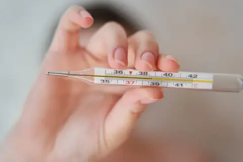 Dłoń trzyma termometr, na którym widać 37,2°C. To może oznaczać wyższą temperaturę pod prawą pachą.
