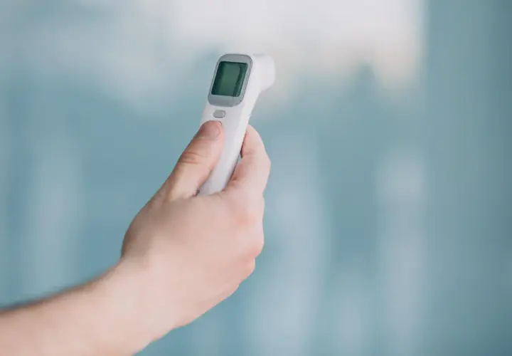 Dłoń trzyma biały termometr bezdotykowy, gotowy do pomiaru temperatury. Prosty sposób na szybkie sprawdzenie gorączki.