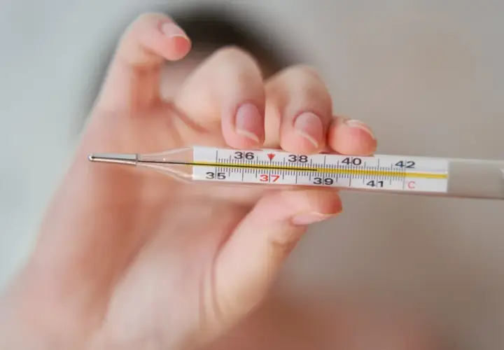 Dłoń trzyma termometr, na którym widać 37,2°C. To może oznaczać wyższą temperaturę pod prawą pachą.