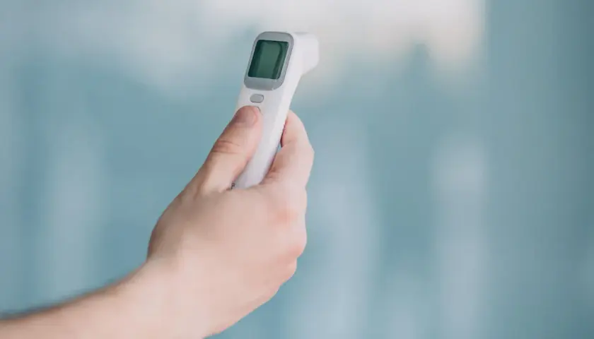 Dłoń trzyma biały termometr bezdotykowy, gotowy do pomiaru temperatury. Prosty sposób na szybkie sprawdzenie gorączki.