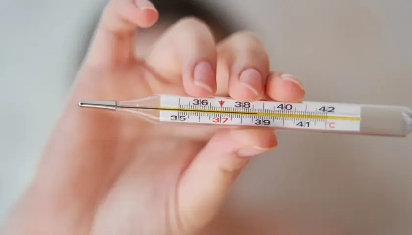Dłoń trzyma termometr, na którym widać 37,2°C. To może oznaczać wyższą temperaturę pod prawą pachą.
