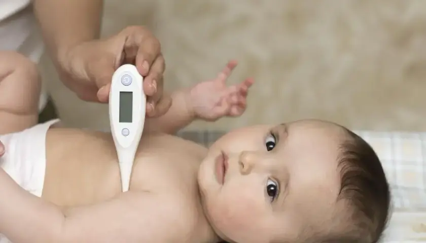 Dziecko leży na plecach, a ręka rodzica mierzy mu temperaturę termometrem pod pachą. To jedno z miejsc, gdzie mierzyć temperaturę u malucha.