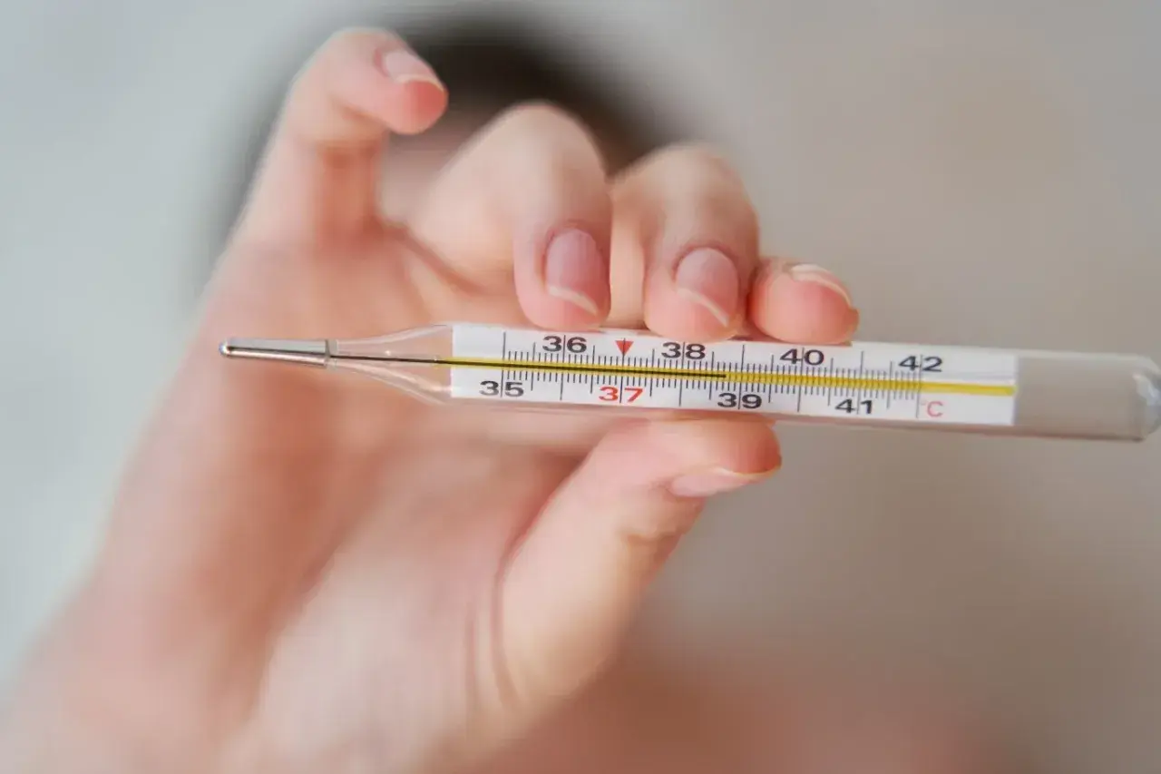Dłoń trzyma termometr, na którym widać 37,2°C. To może oznaczać wyższą temperaturę pod prawą pachą.